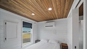 Een slaapkamer met een houten plafond, een bed, een raam met uitzicht en een klein nachtkastje.