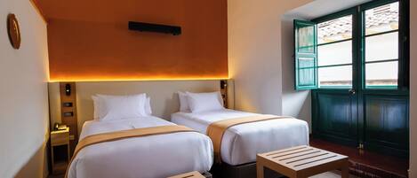 Een hotelkamer met twee bedden, een tafeltje, een nachtkastje en een raam met uitzicht.