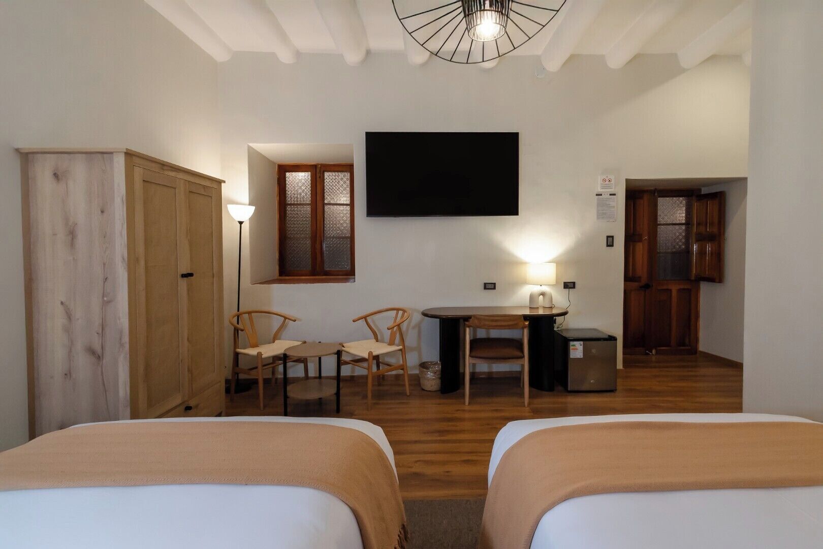 A room with two beds, a desk with a chair, a television, and a wardrobe.