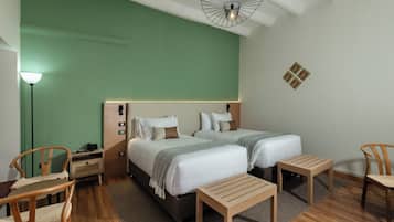A hotel room with two beds, a desk, chairs, a lamp, and a unique ceiling light fixture.