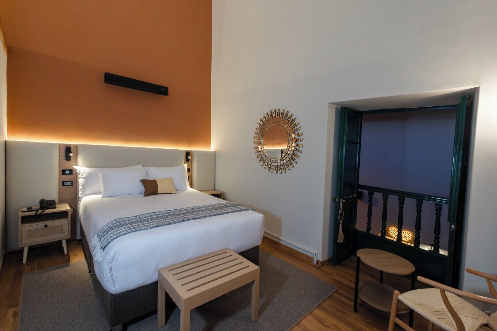 Una habitación de hotel con cama, mesita de noche y un pequeño banco de madera.