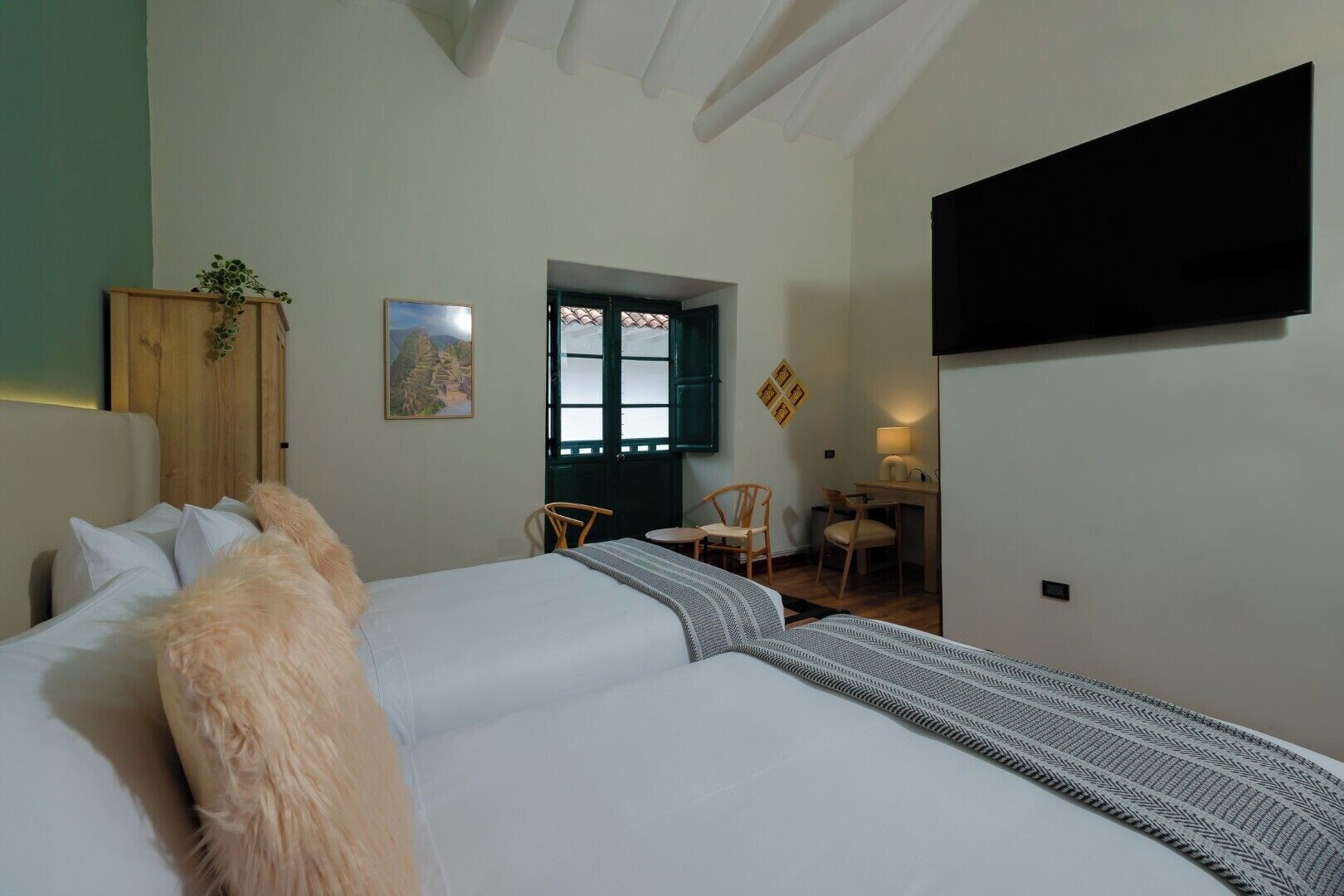 Een slaapkamer met een bed, bureau, stoelen, een televisie en een raam met luiken.