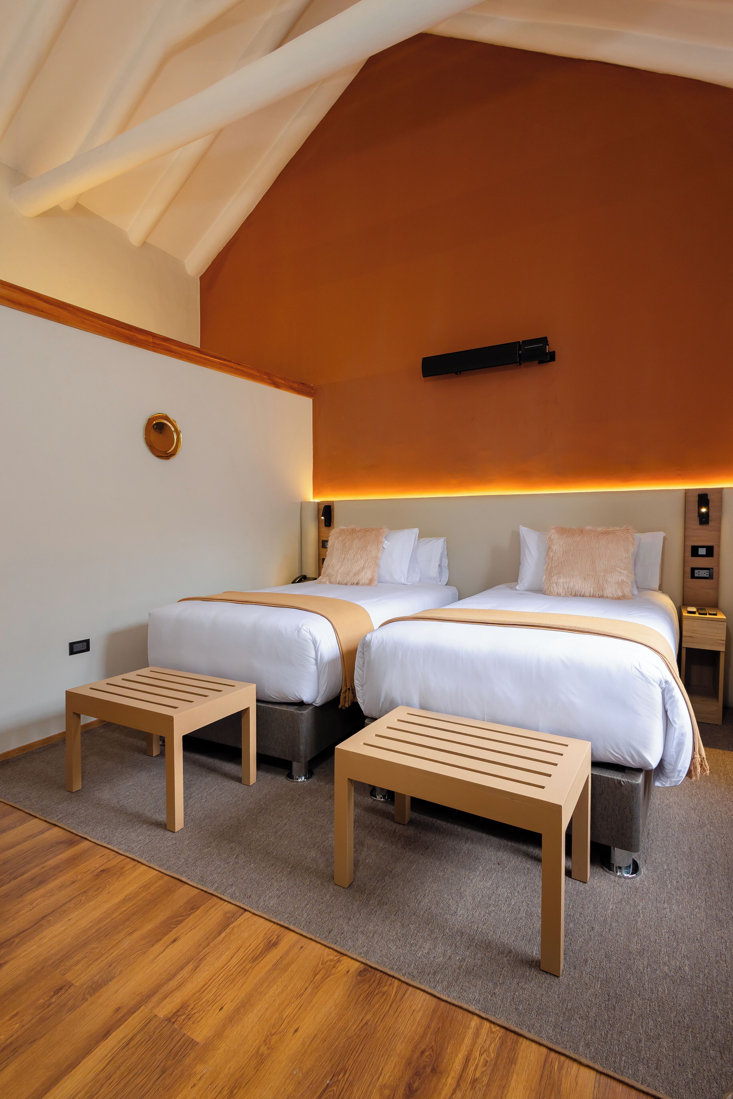 A modern hotel room with two beds, wooden nightstands, and a bench.