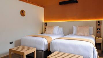 A modern hotel room with two beds, wooden nightstands, and a bench.