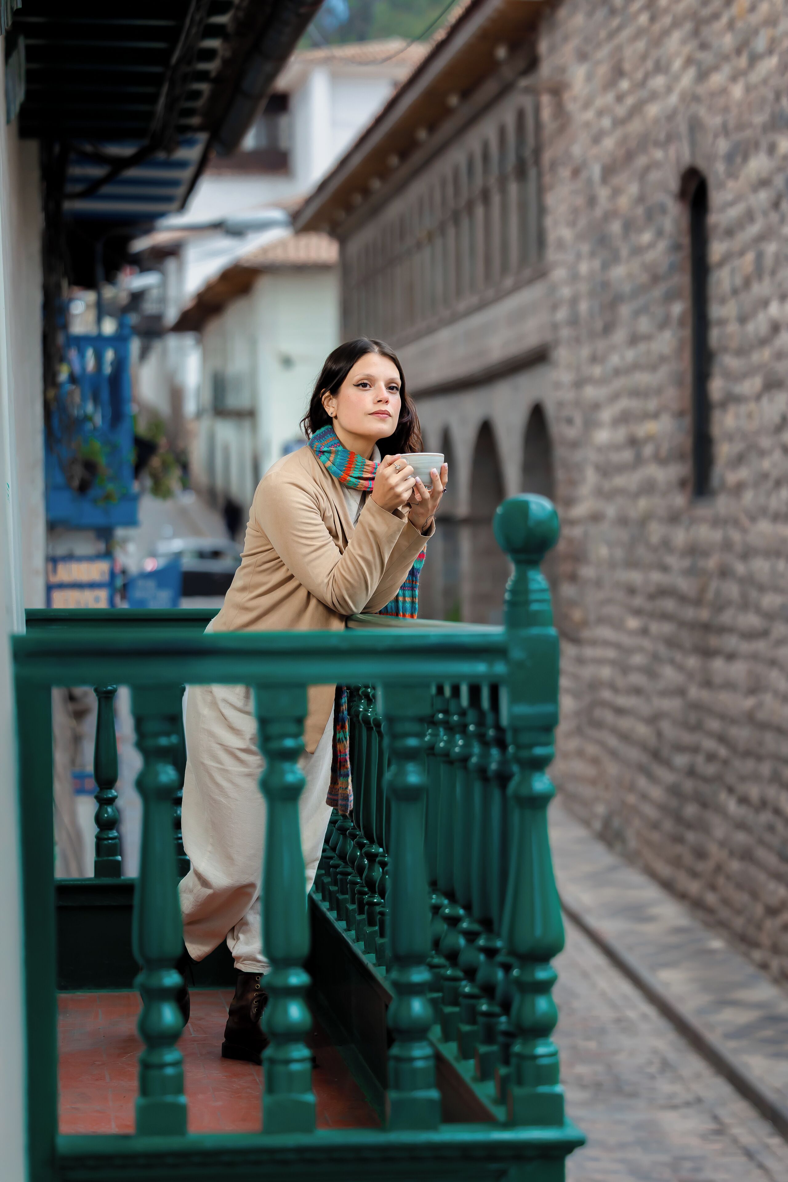 A person leaning on a green railing in a narrow street with stone buildings.