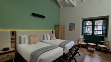 Habitación de hotel con dos camas, una mesita y sillas. Se ve una ventana con vistas a edificios.