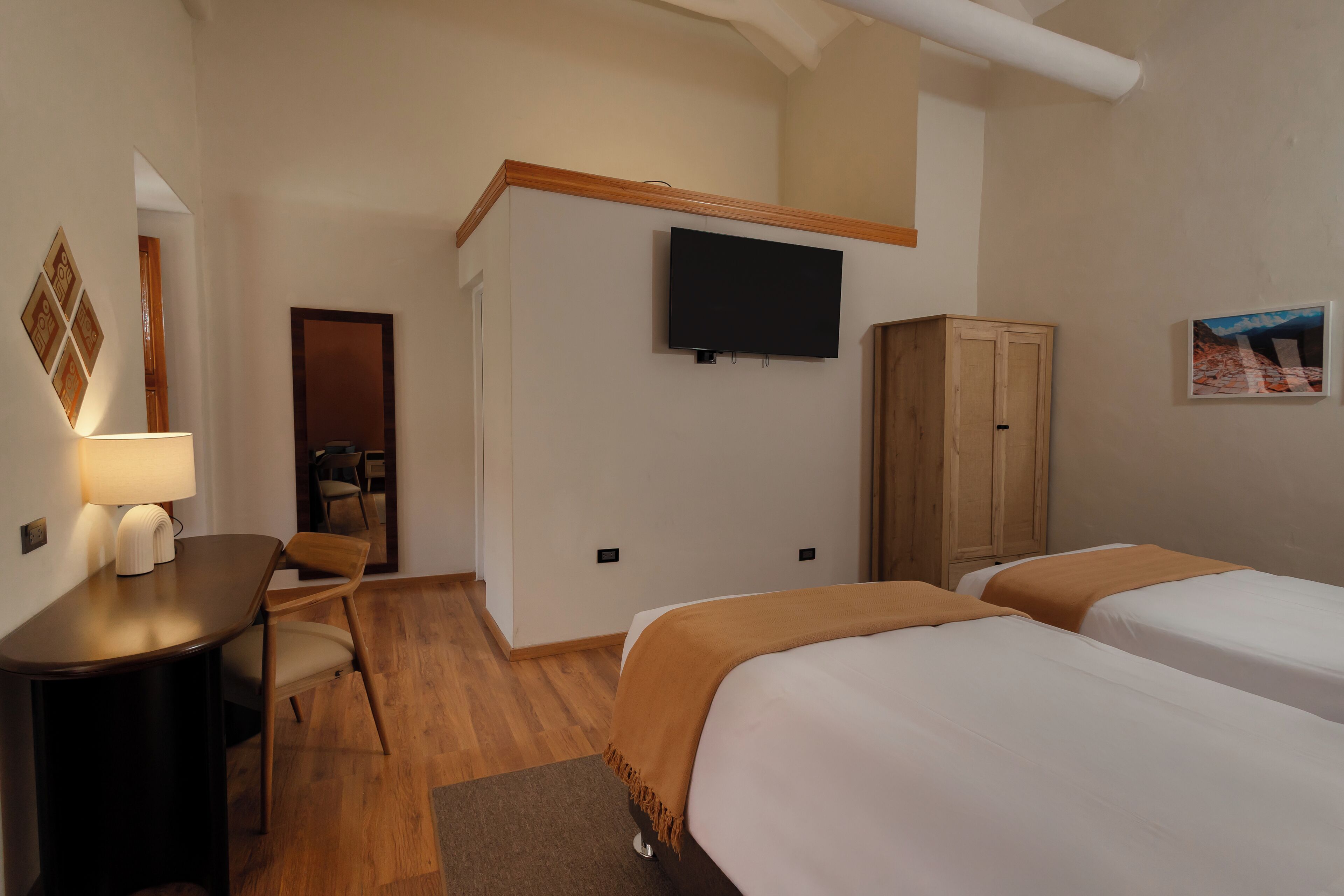 A hotel room with two beds, a desk with a chair, a TV mounted on the wall, and a wooden cabinet.