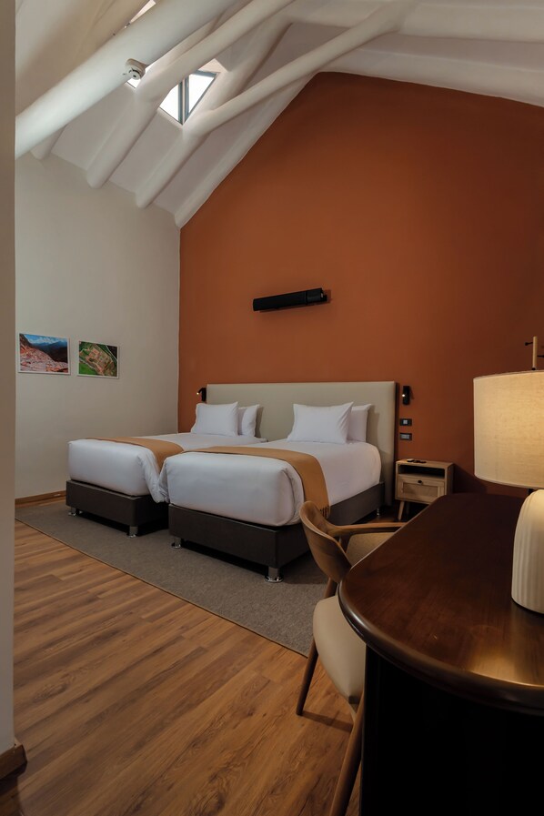 A hotel room with two beds, a wooden floor, a table, and a view of the sky through a skylight. - Sonqori Boutique Hotel (Cusco)