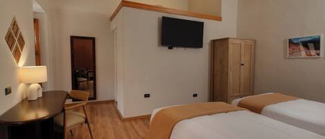 A hotel room with two beds, a desk with a lamp, a television mounted on the wall, and a wooden wardrobe.