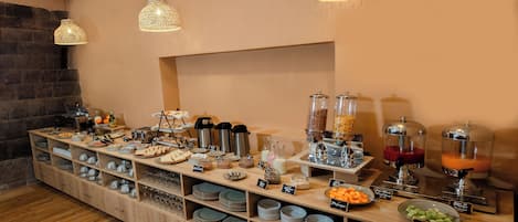 A buffet setup with various food items and beverages, including a fruit bowl, a juice dispenser, and a coffee station.