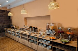 Montaje de bufé con diversas opciones de comida y bebidas, que incluye un bol de frutas, un dispensador de jugo y una estación de café.