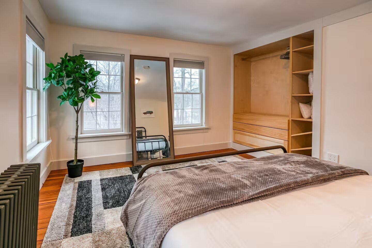 A bedroom with a bed, a potted plant, a mirror, and a wooden wardrobe.