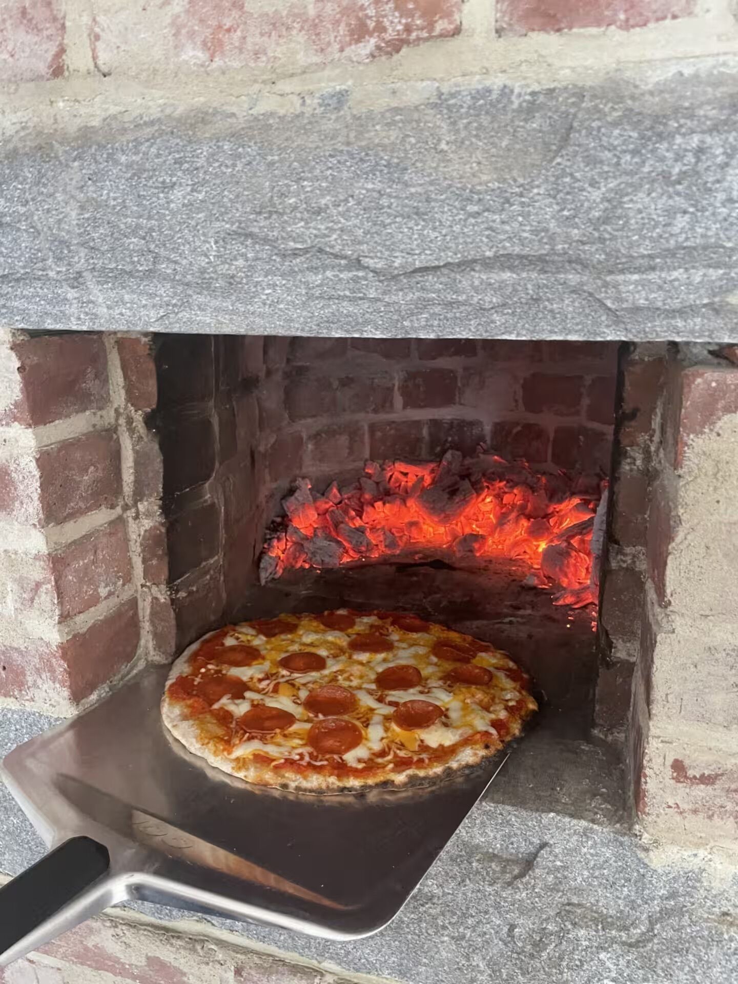 Un horno de pizza con interior de ladrillo y una pizza cocinándose en su interior.