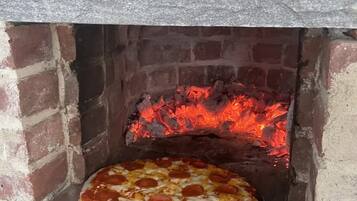 Un horno de pizza con interior de ladrillo y una pizza cocinándose en su interior.