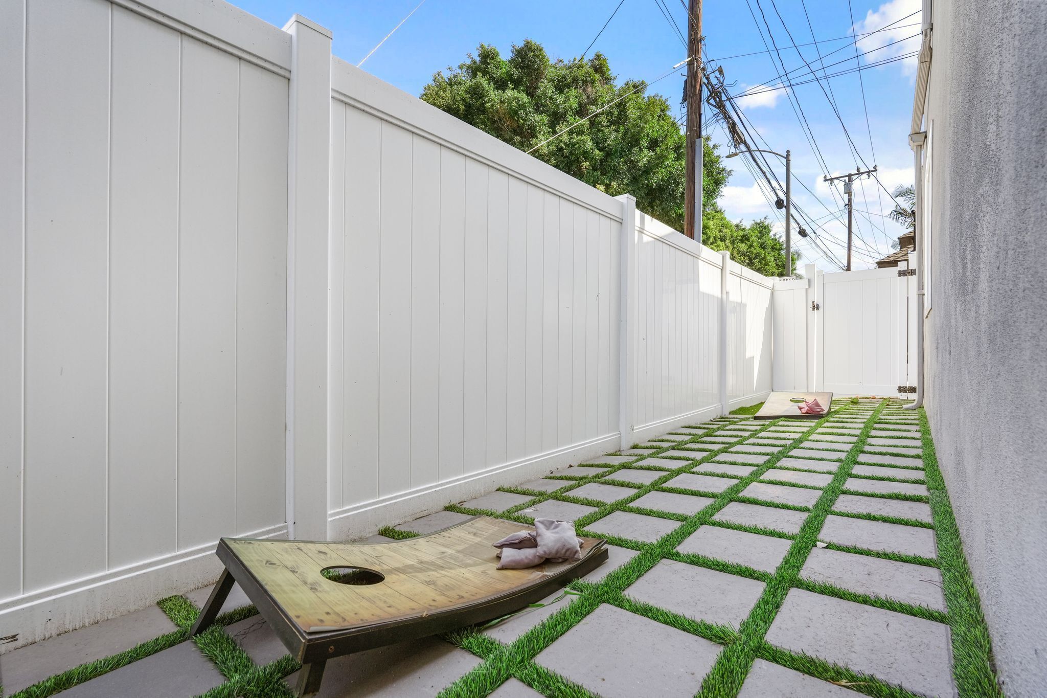 A narrow outdoor space with a white fence, a wooden bench, and a patterned floor.