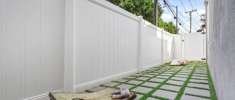 A narrow outdoor space with a white fence, a wooden bench, and a patterned floor.