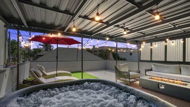 A rooftop patio with a hot tub, outdoor seating, string lights, and a red umbrella.