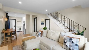 A modern living room with a sofa, a dining table, and a staircase.