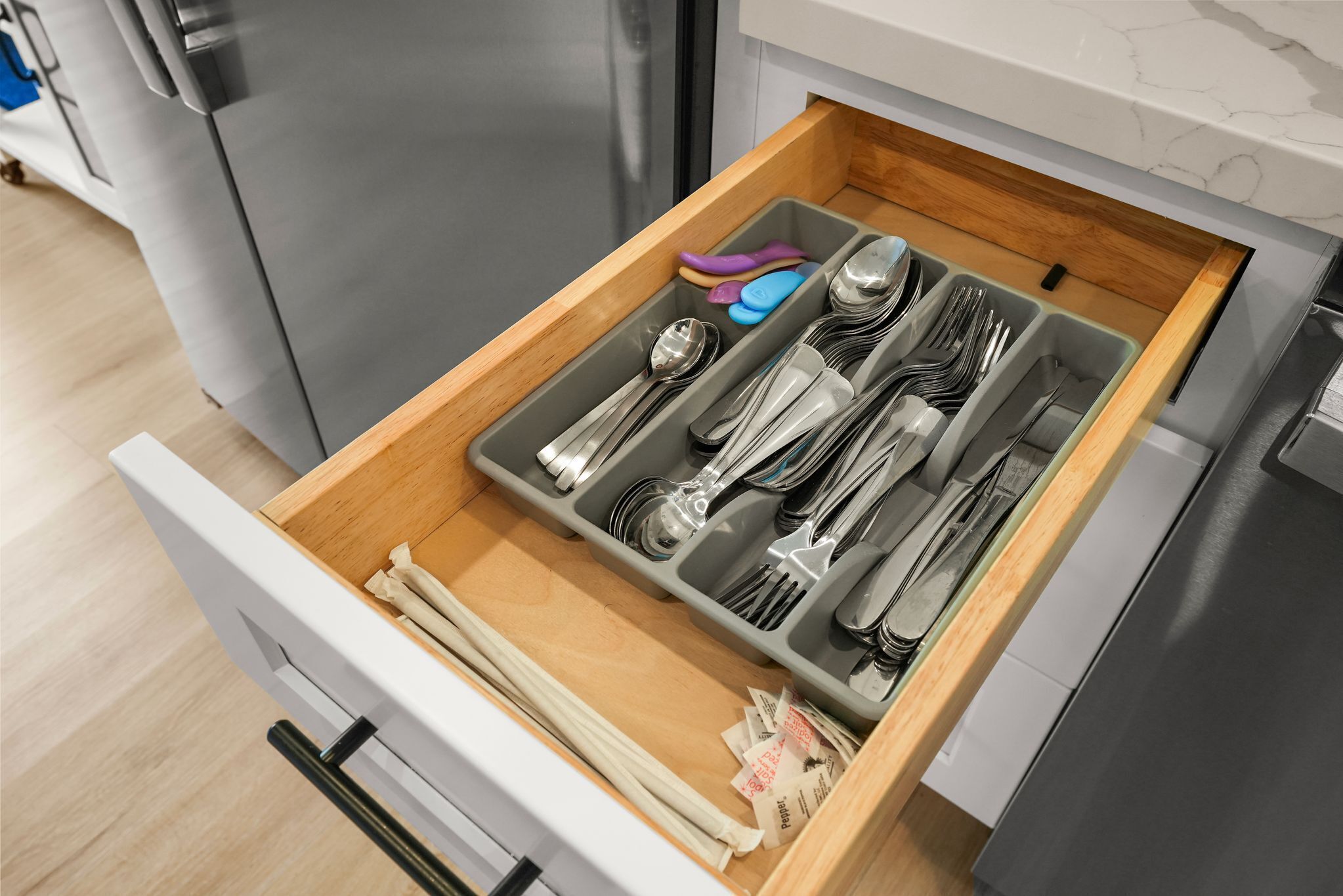 A kitchen drawer with utensils and a small amount of cash.