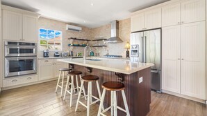 A modern kitchen with white cabinetry, stainless steel appliances, a central island with stools, and a brick accent wall.