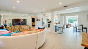 A modern living room with a large white sofa, a flat-screen TV, and a kitchen in the background.