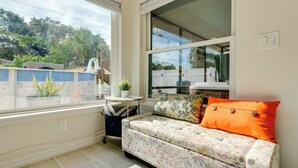 A cozy room with a floral-patterned sofa, a small table with a potted plant, and a large window offering a view of the outdoors.