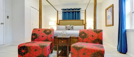 A four-poster bed with a wooden frame and a canopy, flanked by two armchairs with floral upholstery.