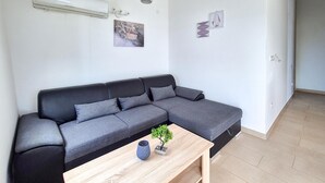 Un salon moderne avec un canapé d’angle gris, une petite table basse en bois et une plante en pot.