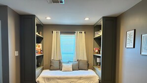 A bedroom with a bed centered under a window, flanked by shelving units with decorative items. - The Cottage at The Stables - Charming 1 bedroom - Sleeps 5 (Vancleave)