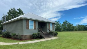 A single-story house with a front porch, a satellite dish, and a well-maintained lawn. - The Cottage at The Stables - Charming 1 bedroom - Sleeps 5 (Vancleave)