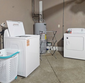 Een wasserette met een voorlader wasmachine en droger, een metalen droogrek en een wasmand.