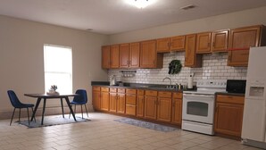 Una cocina con armarios de madera, un refrigerador blanco, una estufa y un comedor con dos sillas.