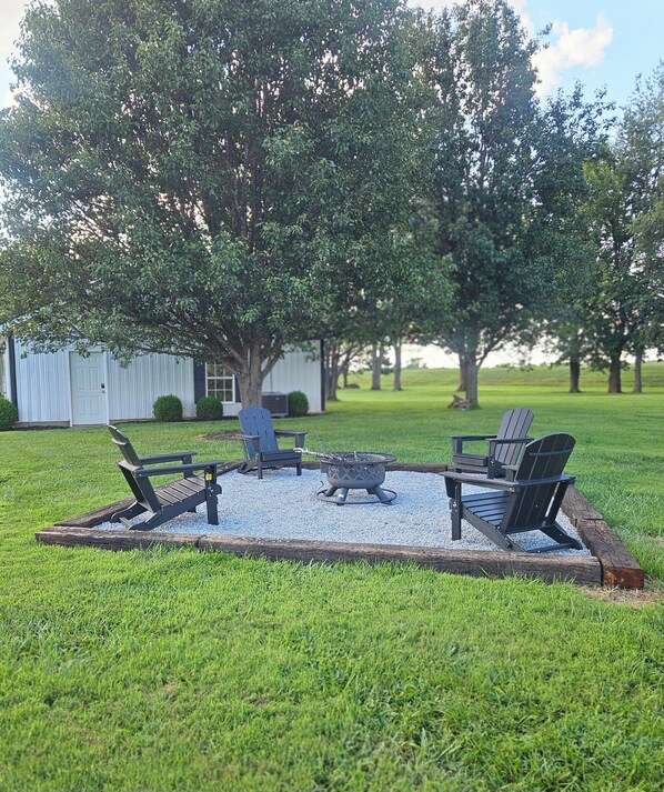 Un espacio al aire libre con césped, una hoguera y cuatro sillas Adirondack.