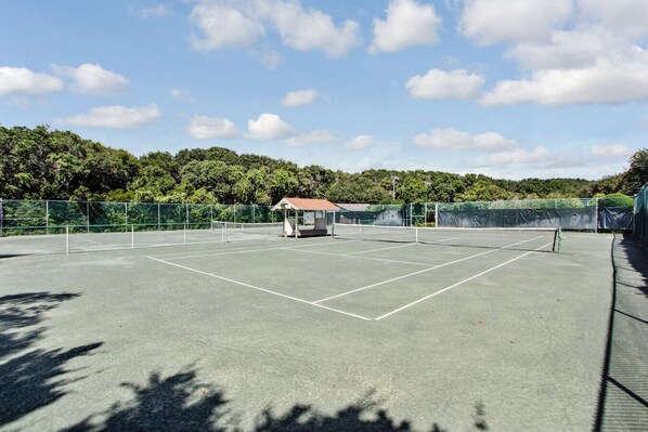 Una cancha de tenis al aire libre con una red, rodeada por una valla y árboles.