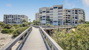 Ein Strandhotel mit einer Holzpromenade, die zum Gebäude führt, umgeben von viel Grün und Palmen.