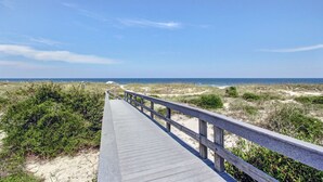 Ein Holzsteg führt zu einem Strand mit Dünen und Meerblick.
