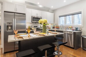 Una cocina moderna con electrodomésticos de acero inoxidable, una isla central con taburetes y un amplio ventanal que proporciona luz natural.