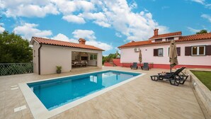 A swimming pool with a tiled deck, a covered patio area with outdoor furniture, and a building with a red-tiled roof. - Cozy home in Sveti Bartol (Sveti Bartol)