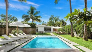 A swimming pool with lounge chairs and umbrellas, surrounded by palm trees and a wooden deck. - Villa Parque Pickleball/Volleyball/Bball/MiniGolf (Miami)
