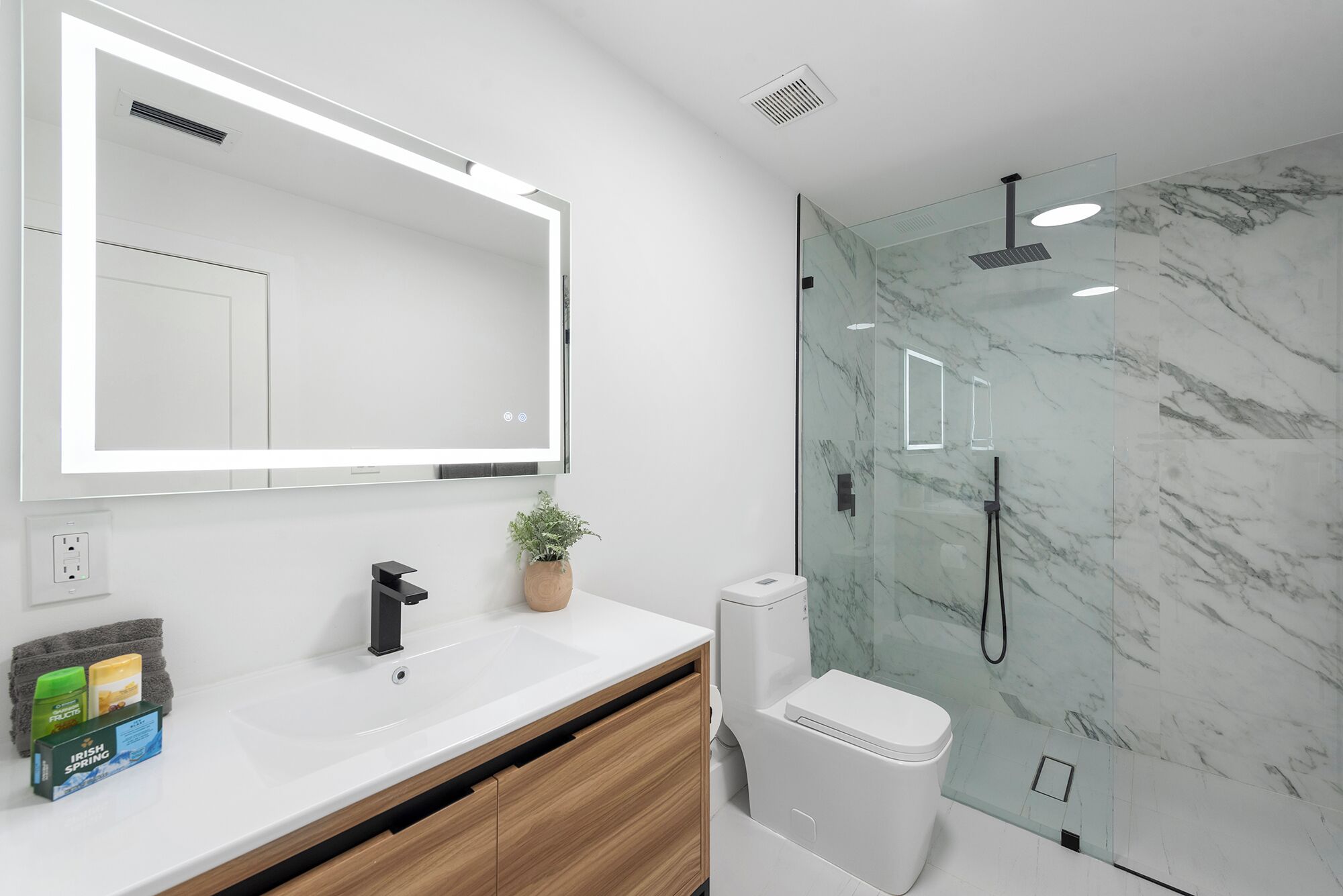 A modern bathroom with a large mirror, a glass shower enclosure, and a white sink with a wooden vanity.
