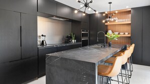 A modern kitchen with a large island, dark cabinetry, and a unique chandelier. - Villa Parque Pickleball/Volleyball/Bball/MiniGolf (Miami)