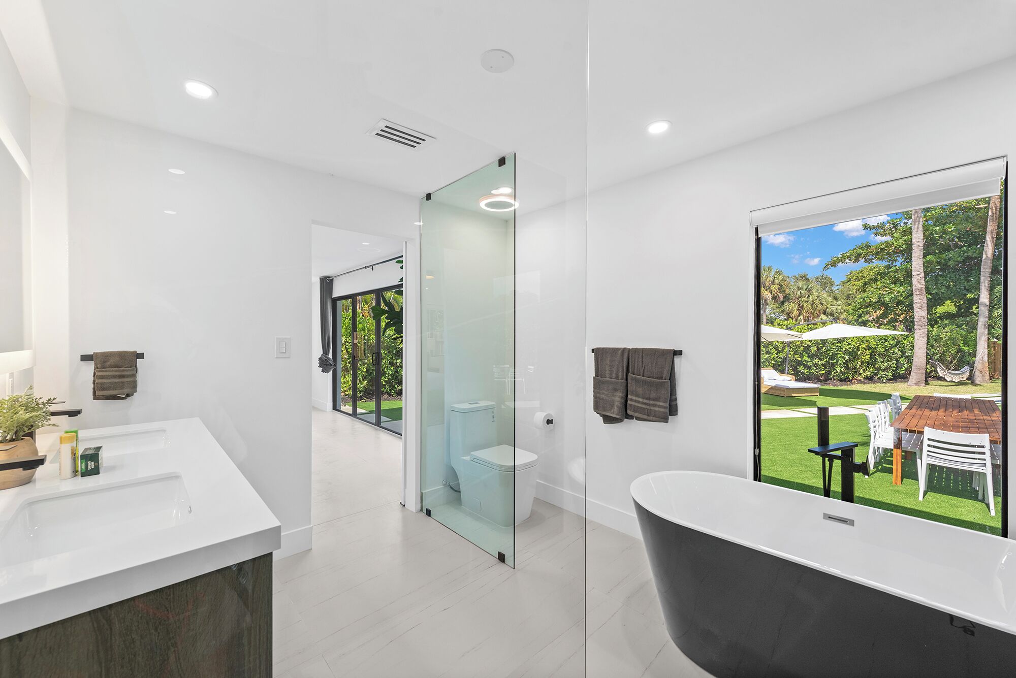 A modern bathroom with a large bathtub, a glass shower enclosure, and a view of a garden through a large window.