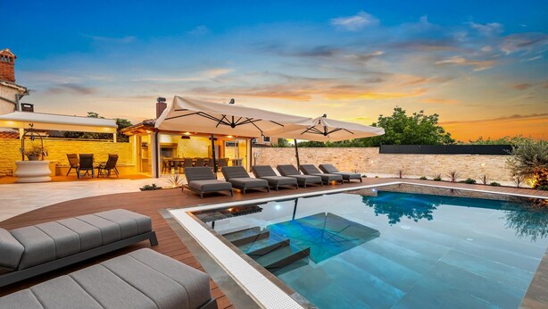 A modern outdoor pool area with lounge chairs, a covered seating area, and a stone wall.