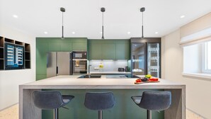 A modern kitchen with a central island, bar stools, stainless steel appliances, and a glass display cabinet.