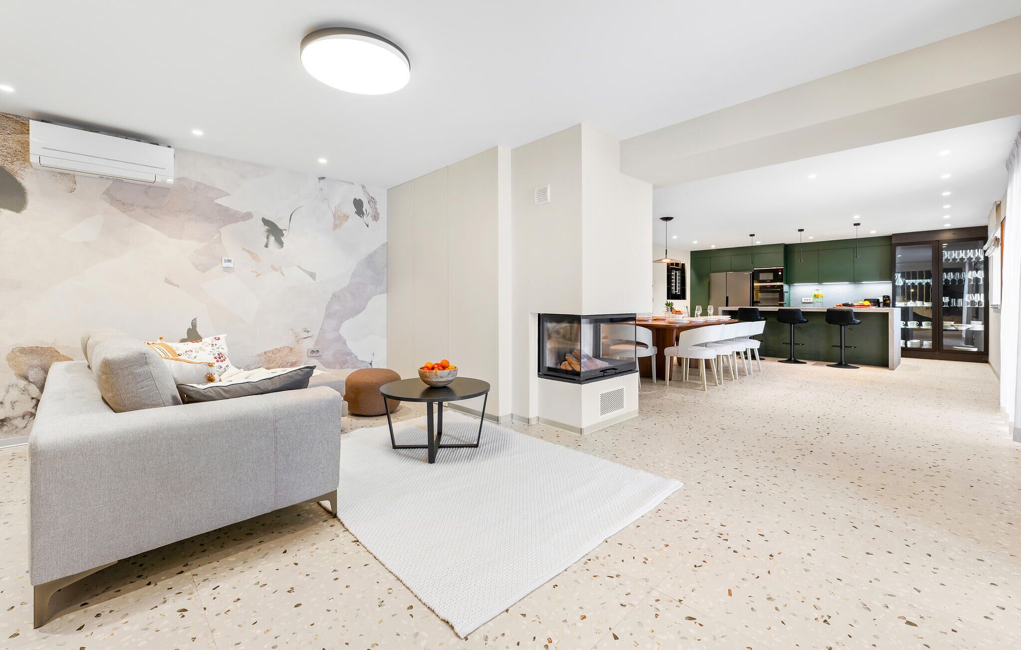 Een moderne woonkamer met een bank, een salontafel en een open haard. Er is een keukenhoek met een eettafel en stoelen.