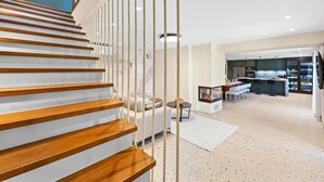 A modern interior with a wooden staircase, a dining area, kitchen, and a living space with a fireplace.