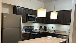 A modern kitchen with dark cabinetry, a stainless steel refrigerator, a microwave, a coffee maker, and two bar stools. - Near Universal studios, Scenic Pool Balcony, no resort fee, shuttle option. (Orlando)