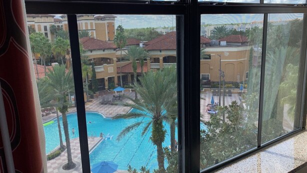 A view of a swimming pool with palm trees and a building in the background. - Near Universal studios, Scenic Pool Balcony, no resort fee, shuttle option. (Orlando)