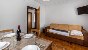 Un coin repas avec une table dressée pour deux personnes, une bouteille de vin et un canapé en arrière-plan.