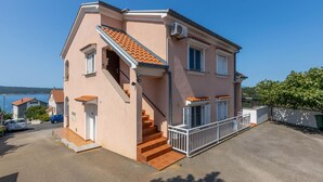 Une maison à deux étages avec un escalier menant à l’étage supérieur, un balcon doté d’une balustrade et une vue sur la mer.